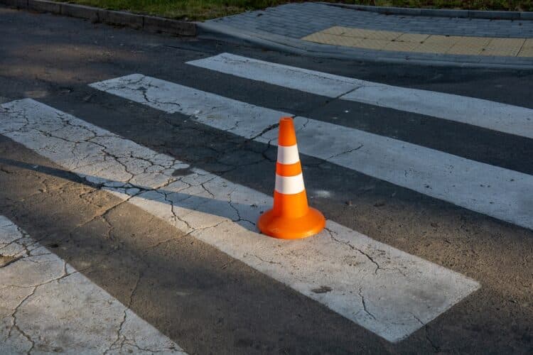 A traffic cone on a cracked pedestrian crossing.