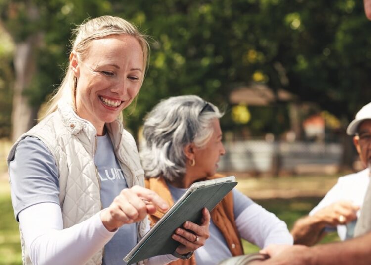 Smile, women and reading with tablet outdoor for charity, online checklist and community service. People, parcel and digital for donation inventory, humanitarian outreach and ngo agenda of food drive